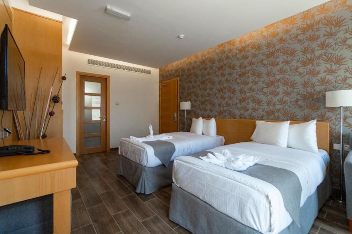 Habitació d'hotel amb dos llits, una taula de treball, un televisor i una porta.