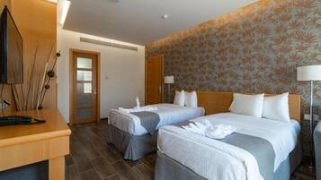 A hotel room with two beds, a desk, a TV, and a door.