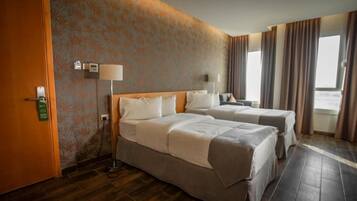 Quarto de hotel com duas camas, piso de madeira, parede estampada e janela com cortinas.