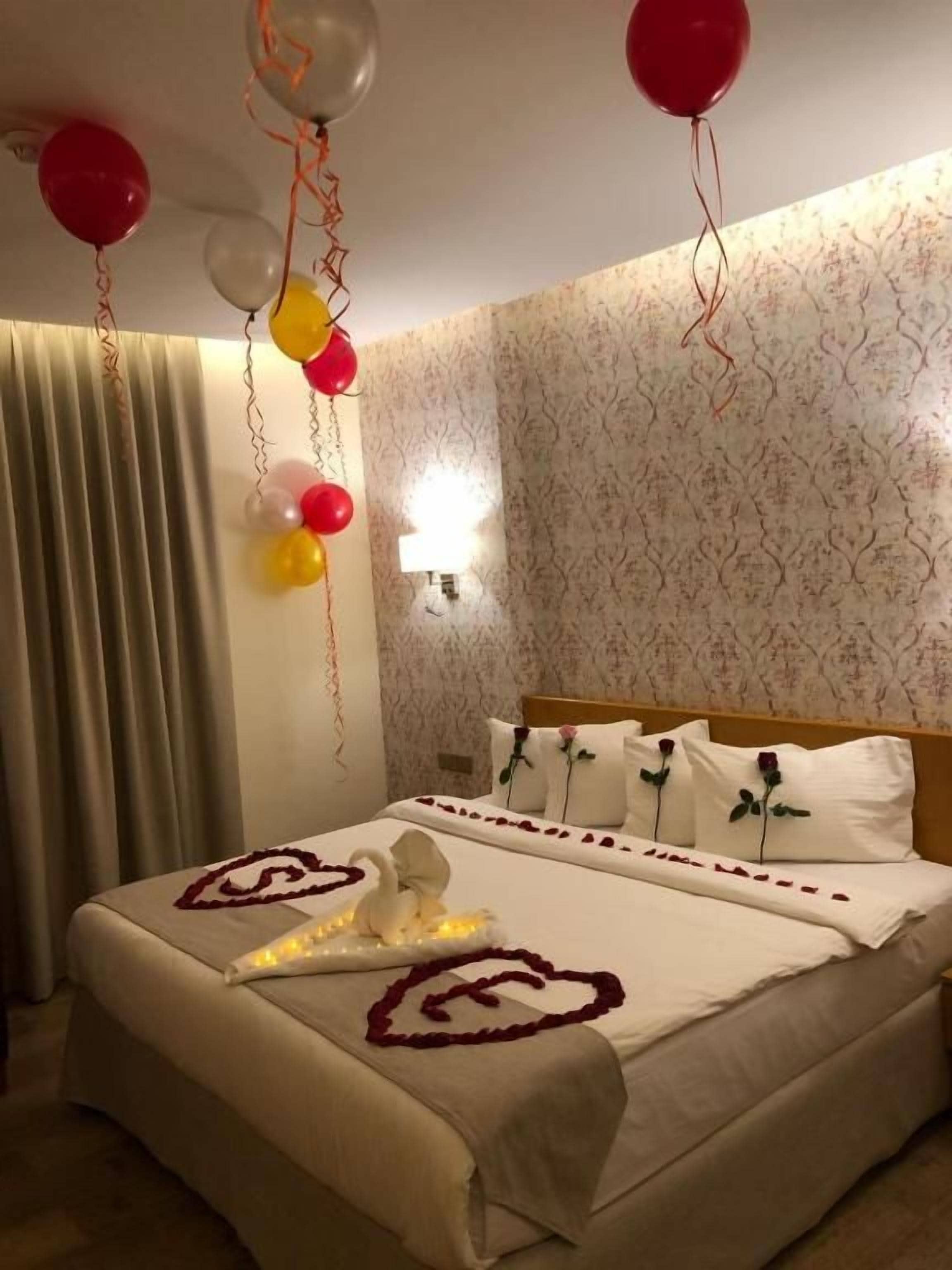 Ein Hotelzimmer mit einem Bett, Kissen, einer Wandleuchte und Luftballons.