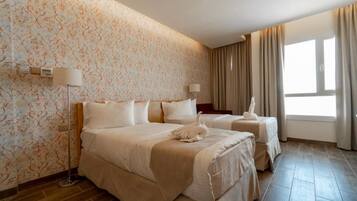 A hotel room with two beds, a patterned wallpaper, a floor lamp, and a window with curtains.