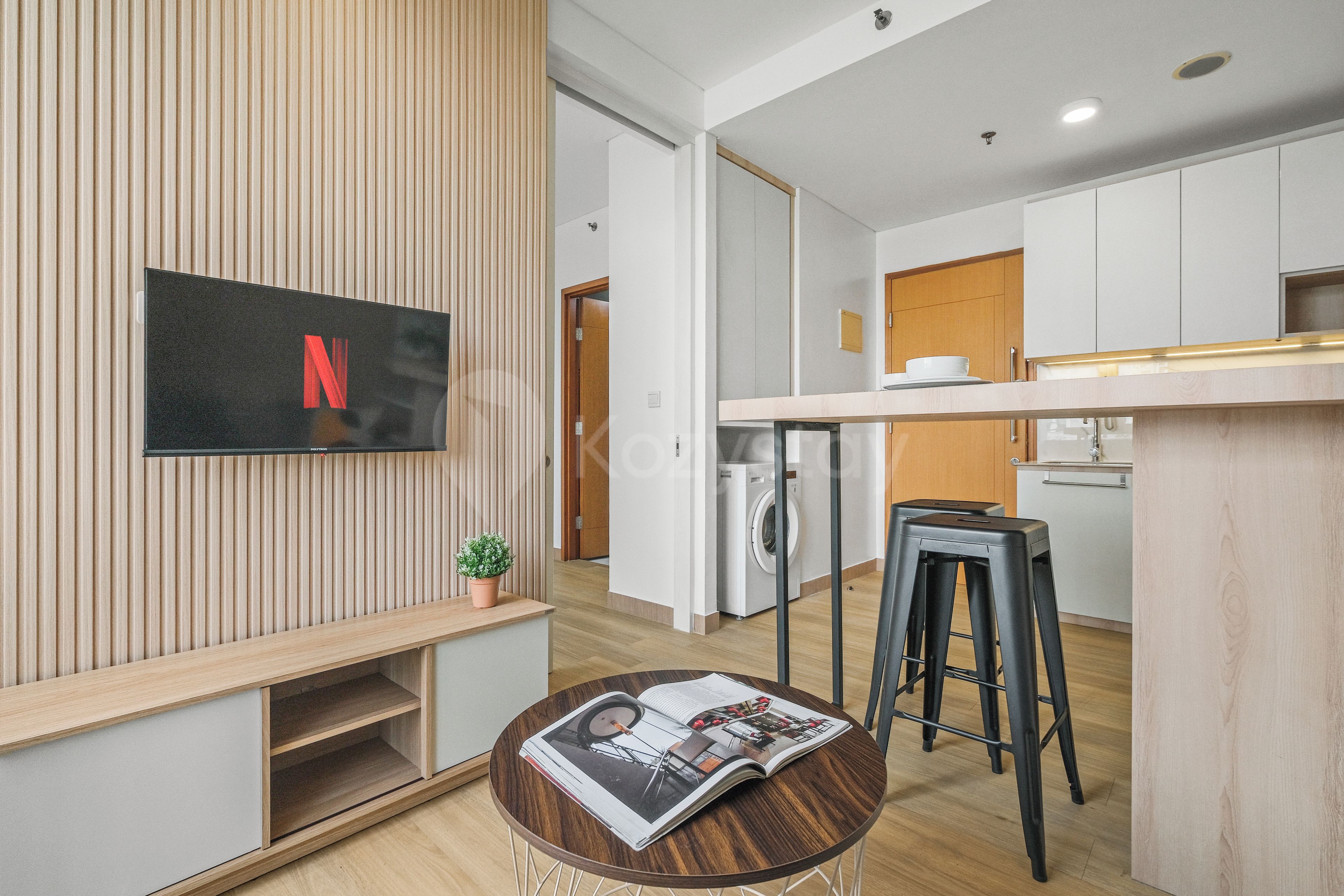 Una cocina moderna con lavadora integrada, un banco de madera y una mesa redonda con una revista.