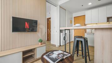 Una cocina moderna con lavadora integrada, un banco de madera y una mesa redonda con una revista.
