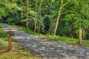 A gravel path leading through a wooded area with signs indicating a retreat and private property. - Hothouse Creek Retreat - Fishing Access, Firepit & Large Outdoor Space (Mineral Bluff)
