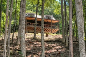 A cabin with a wooden exterior, multiple levels, and a balcony, surrounded by a forested area. - Hothouse Creek Retreat - Fishing Access, Firepit & Large Outdoor Space (Mineral Bluff)