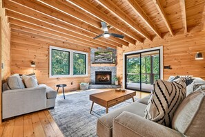 A cozy cabin interior with a stone fireplace, wooden walls, and large windows. - Hothouse Creek Retreat - Fishing Access, Firepit & Large Outdoor Space (Mineral Bluff)