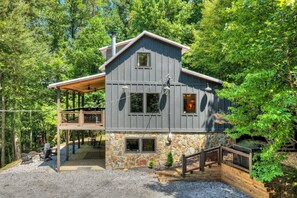 A two-story building with a stone foundation, a covered porch, and a stone fireplace. - Hothouse Creek Retreat - Fishing Access, Firepit & Large Outdoor Space (Mineral Bluff)