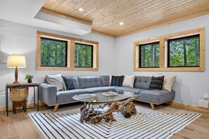 Een moderne woonkamer met een grijze modulaire bank, een glazen salontafel en een houten plafond.