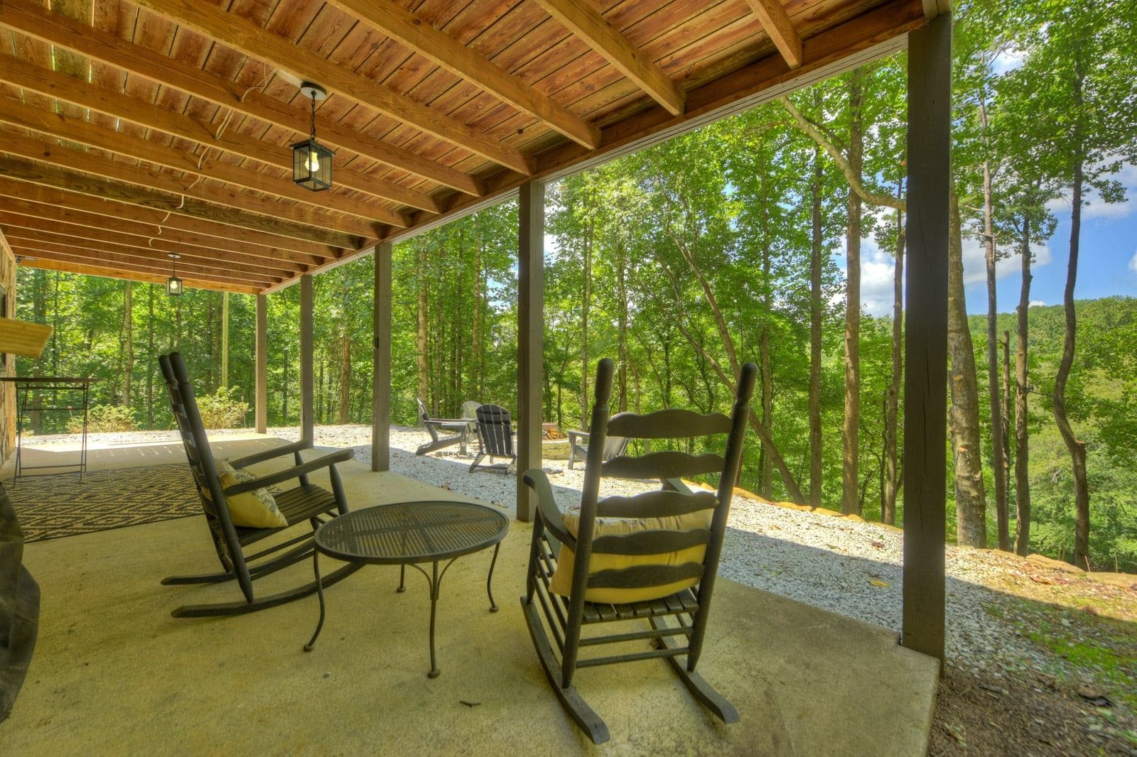 Eine überdachte Terrasse im Freien mit Holzbalken, einem Tisch und zwei Schaukelstühlen.