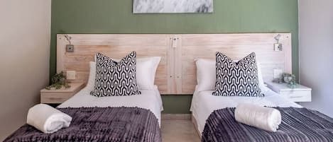 A hotel room with two beds, a green wall, and a ceiling light.