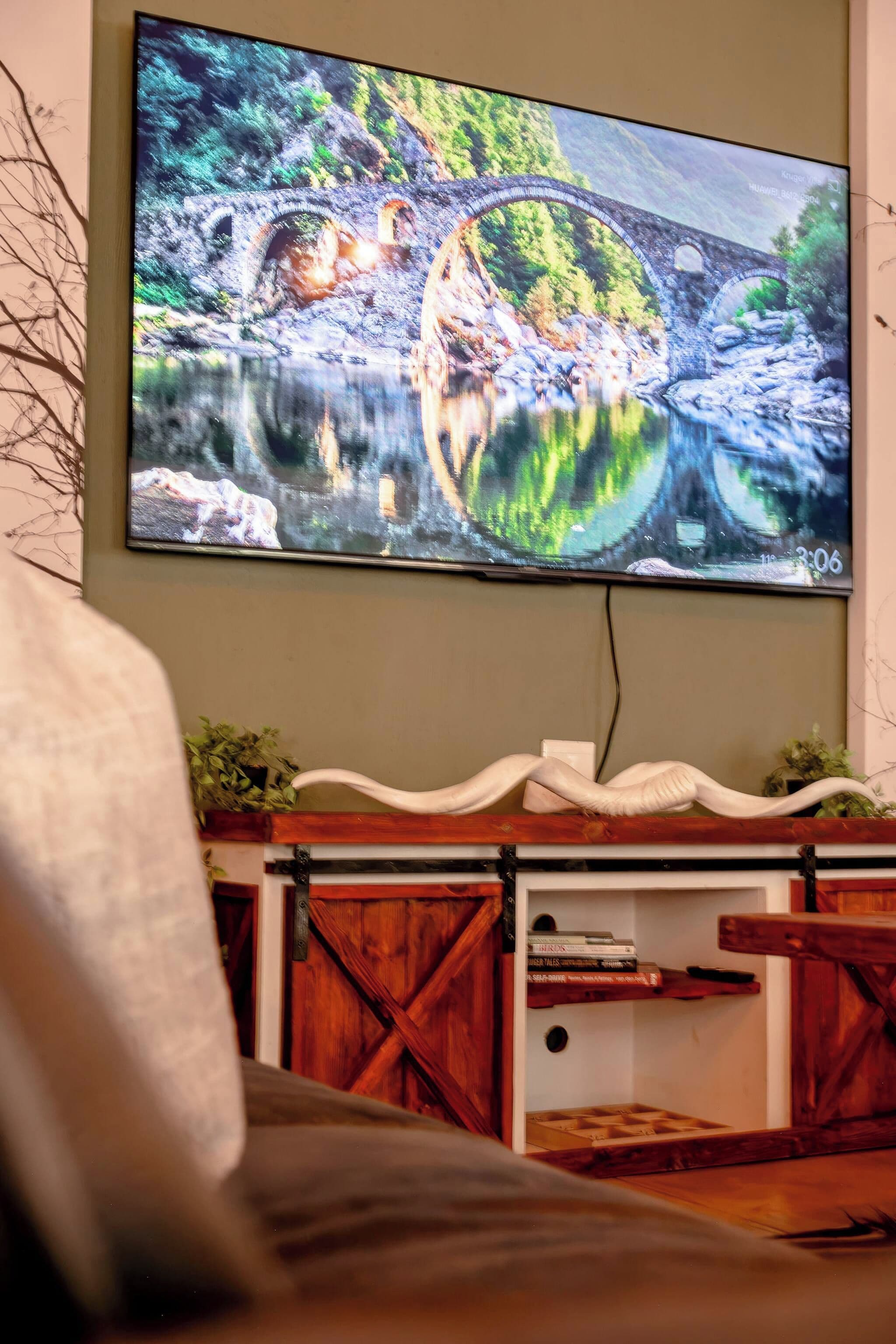 Een flatscreen televisie aan de muur, waarop een mooi beeld van een brug over een rivier te zien is.