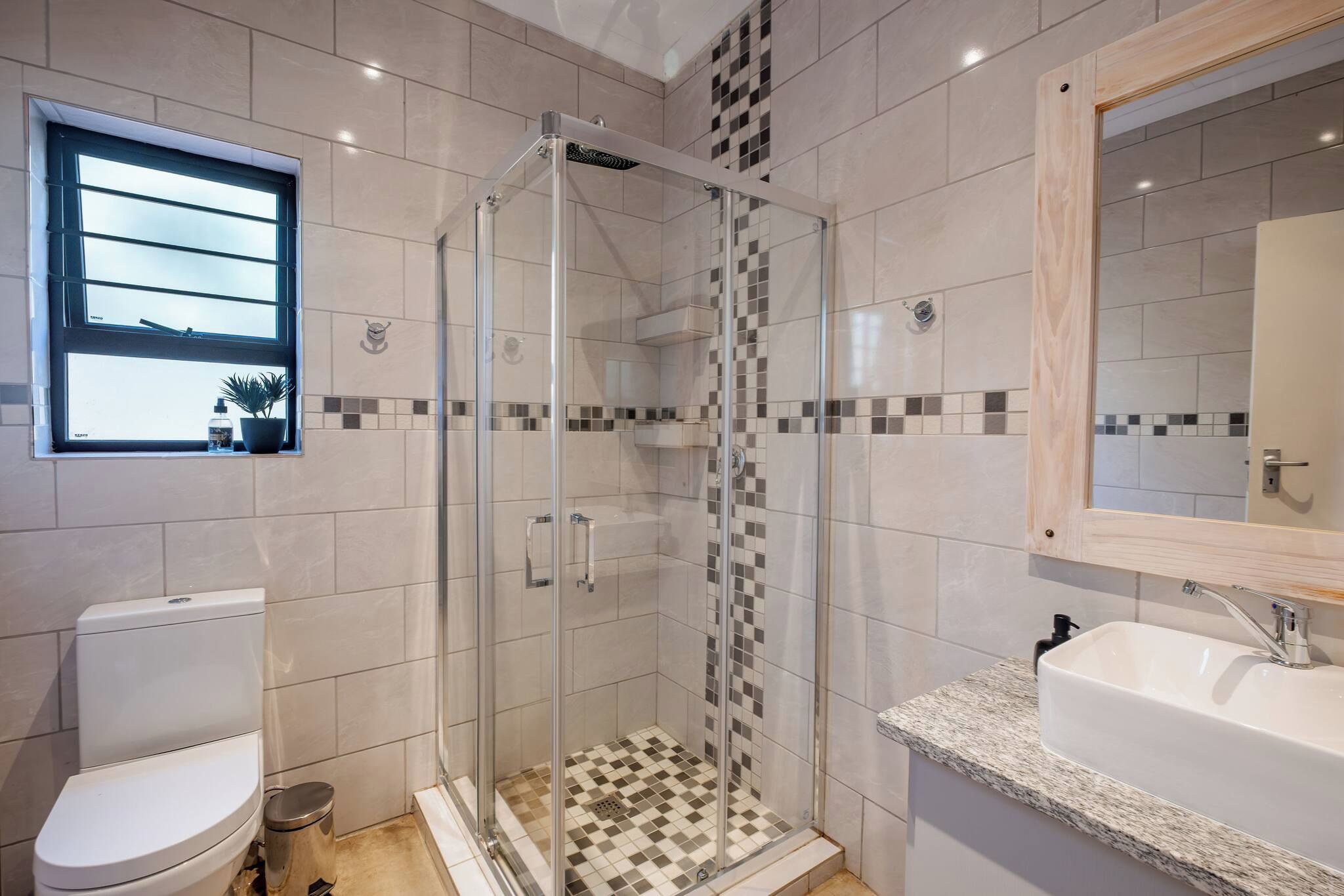 A modern bathroom with a glass-enclosed shower, a toilet, and a sink with a marble countertop.