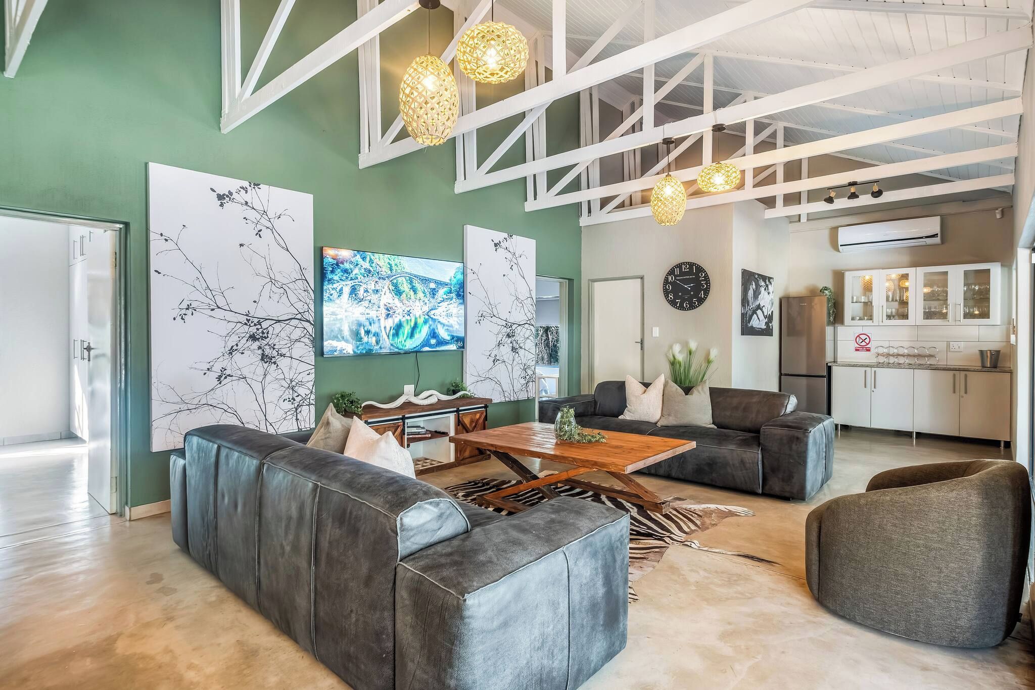 A spacious living area with a large sofa, a coffee table, and a dining table. There are decorative wall art pieces and pendant lights.