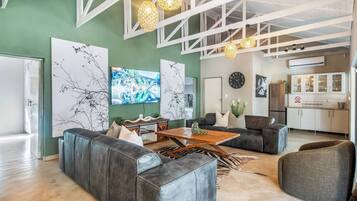 A spacious living area with a large sofa, a coffee table, and a dining table. There are decorative wall art pieces and pendant lights.