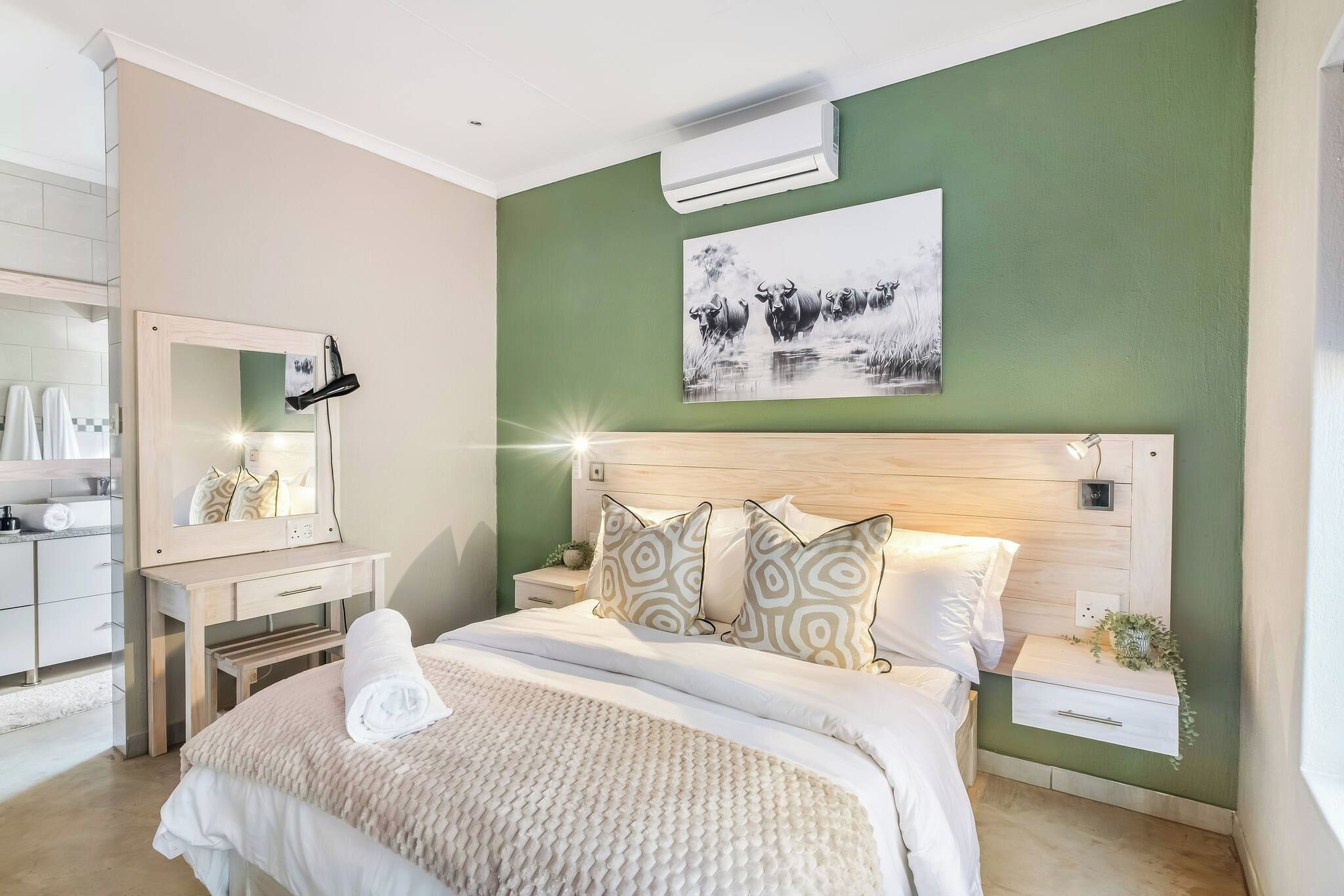A bedroom with a bed, a bedside table, a nightstand, a mirror, and a wall-mounted air conditioner.