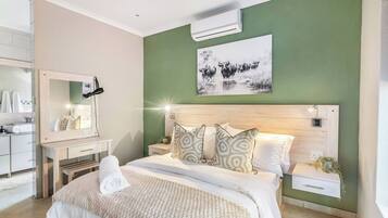 A bedroom with a bed, a bedside table, a nightstand, a mirror, and a wall-mounted air conditioner.