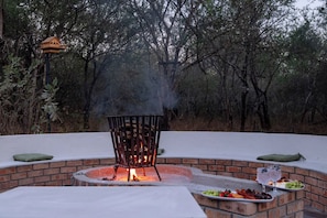 Un pozo de fuego al aire libre con un banco y una mesa con comida y bebidas.