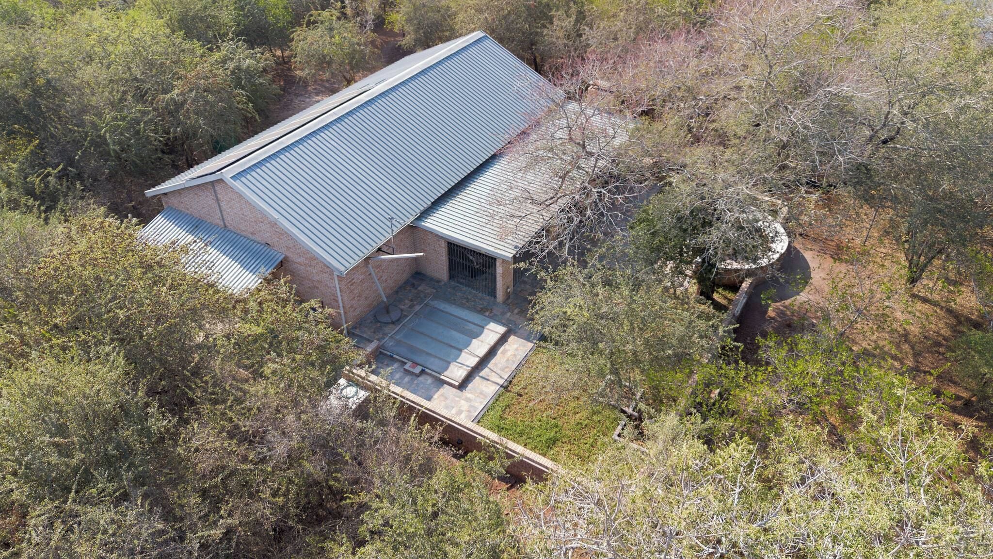A single-story building with a sloped roof, surrounded by dense shrubbery and trees.