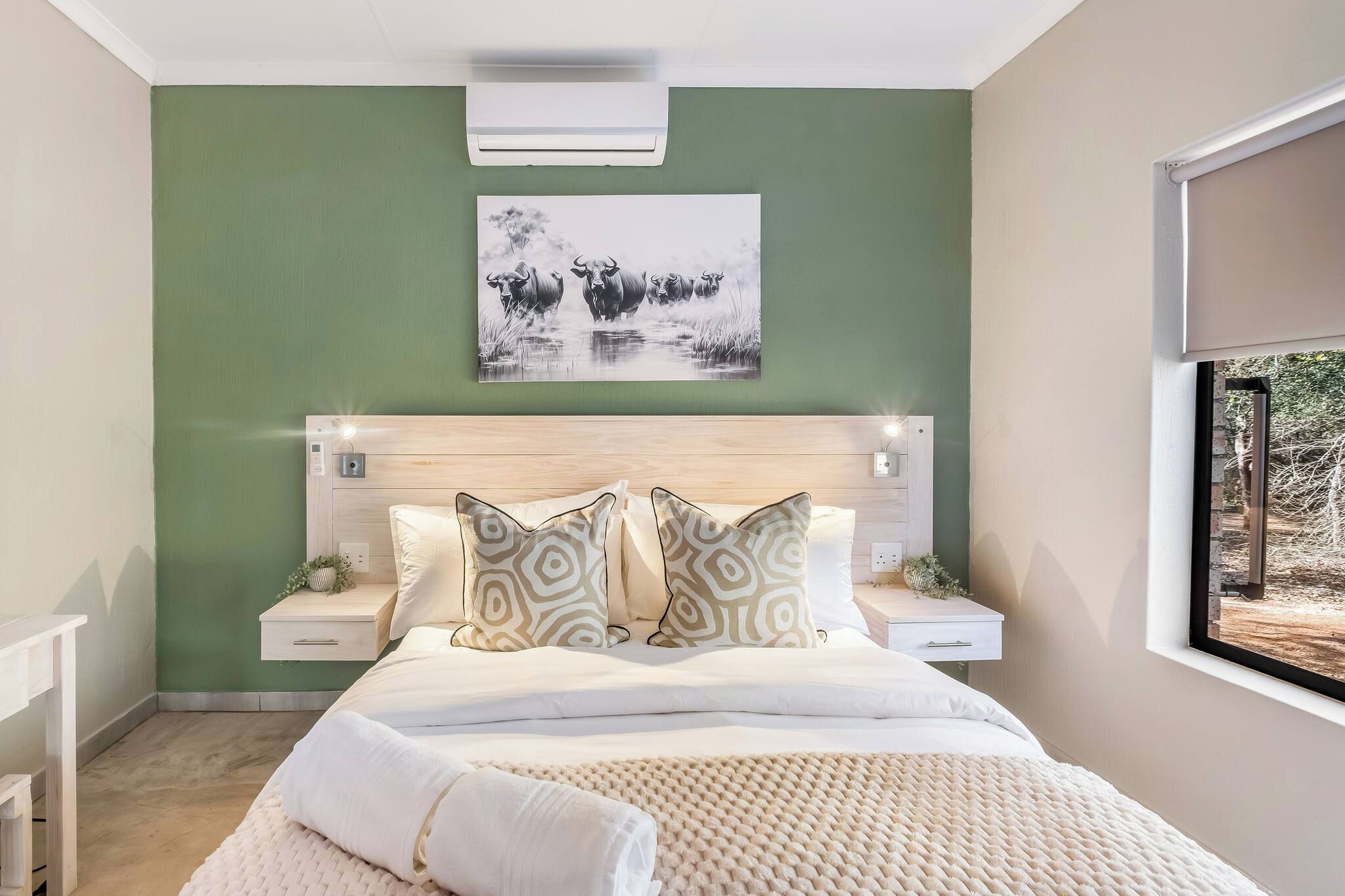 A bedroom with a bed, bedside tables, a headboard, a wall-mounted air conditioner, and a window with a view.