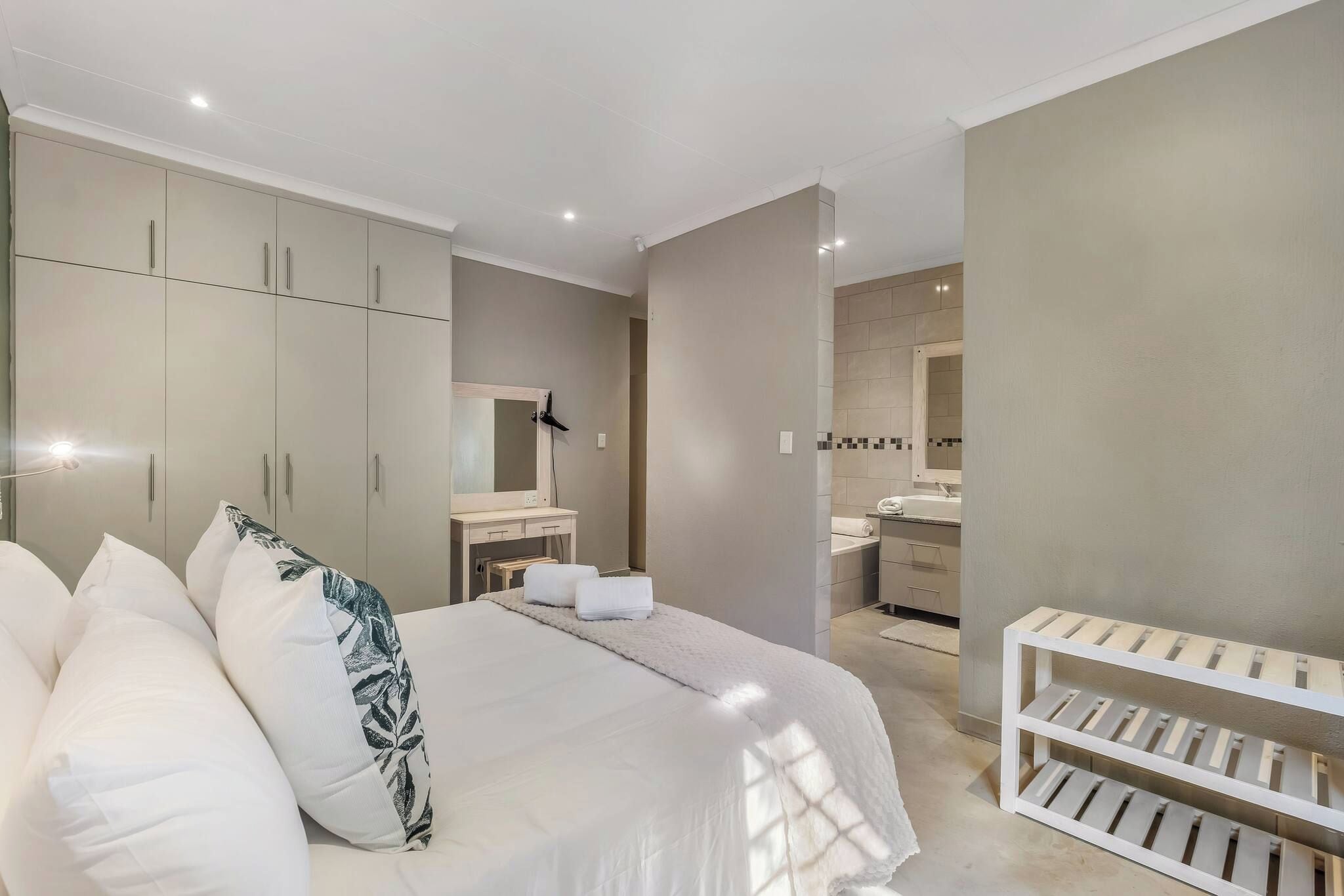 A bedroom with a bed, bedside tables, a wardrobe, a bathroom with a sink and mirror, and a crib.