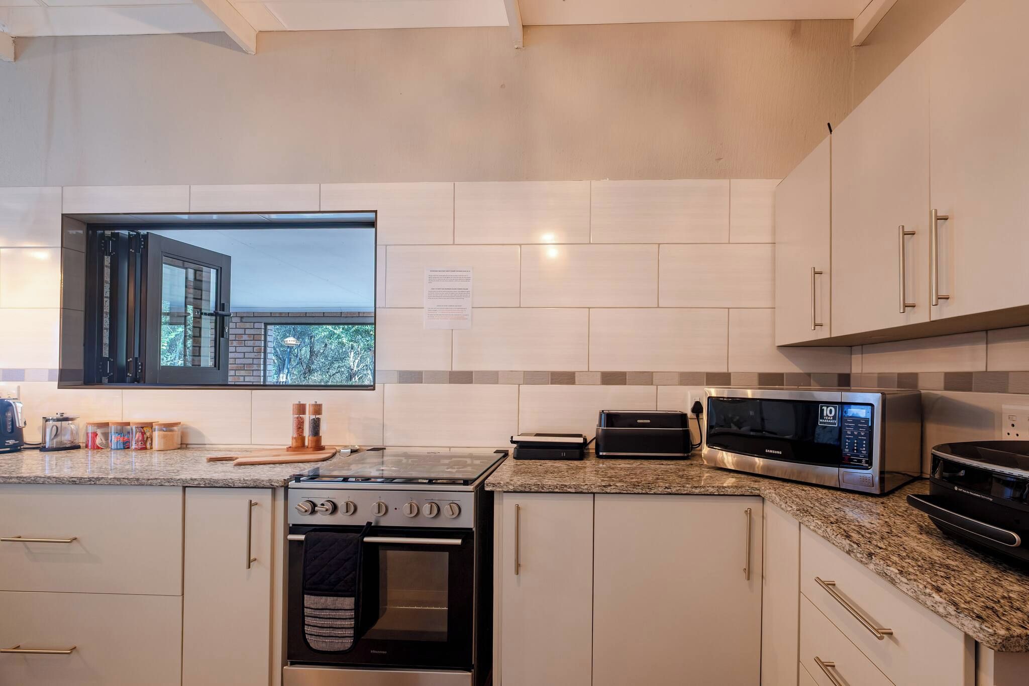 A modern kitchen with a gas stove, oven, microwave, and a window with a view of trees.