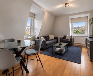 A modern living room with a glass dining table, two sofas, a coffee table, and a view of buildings through large windows. - Soho City Canvas • Stylish 2BR • Sleeps 4 (London)