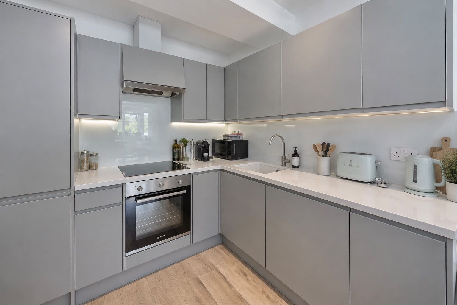 A modern kitchen with grey cabinetry, a built-in oven, a microwave, a kettle, and a toaster on the countertop.
