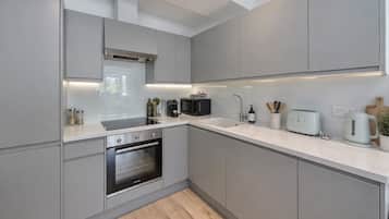 A modern kitchen with grey cabinetry, a built-in oven, a microwave, a kettle, and a toaster on the countertop.
