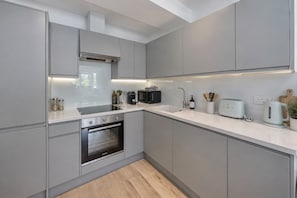 A modern kitchen with grey cabinetry, a built-in oven, a microwave, a kettle, and a toaster on the countertop. - Soho City Canvas • Stylish 2BR • Sleeps 4 (London)