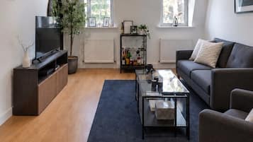 A modern living room with a flat-screen TV, a sofa, a coffee table, and a bookshelf.