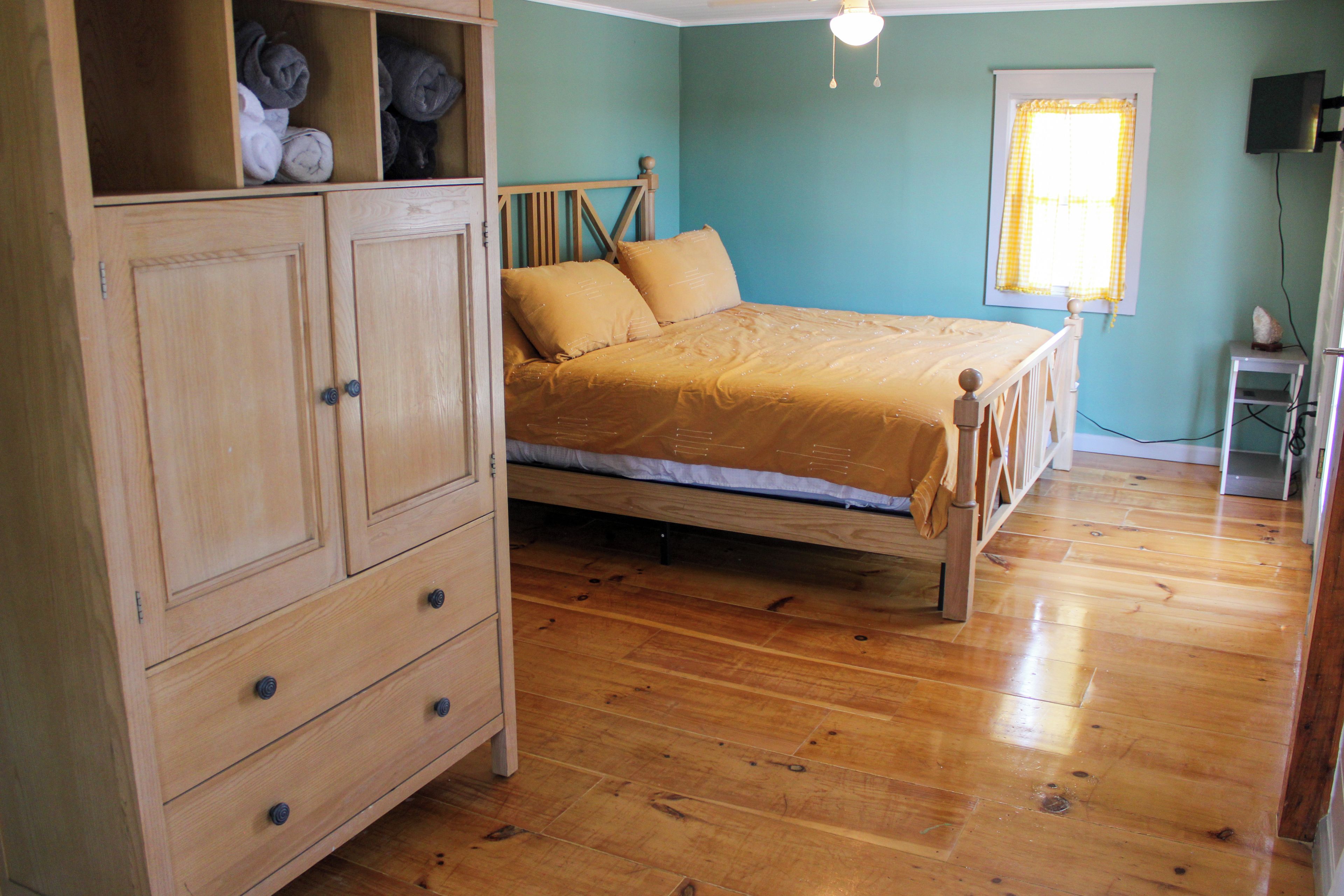 Un dormitorio con una cama de madera, un armario y un ventanal con cortinas.