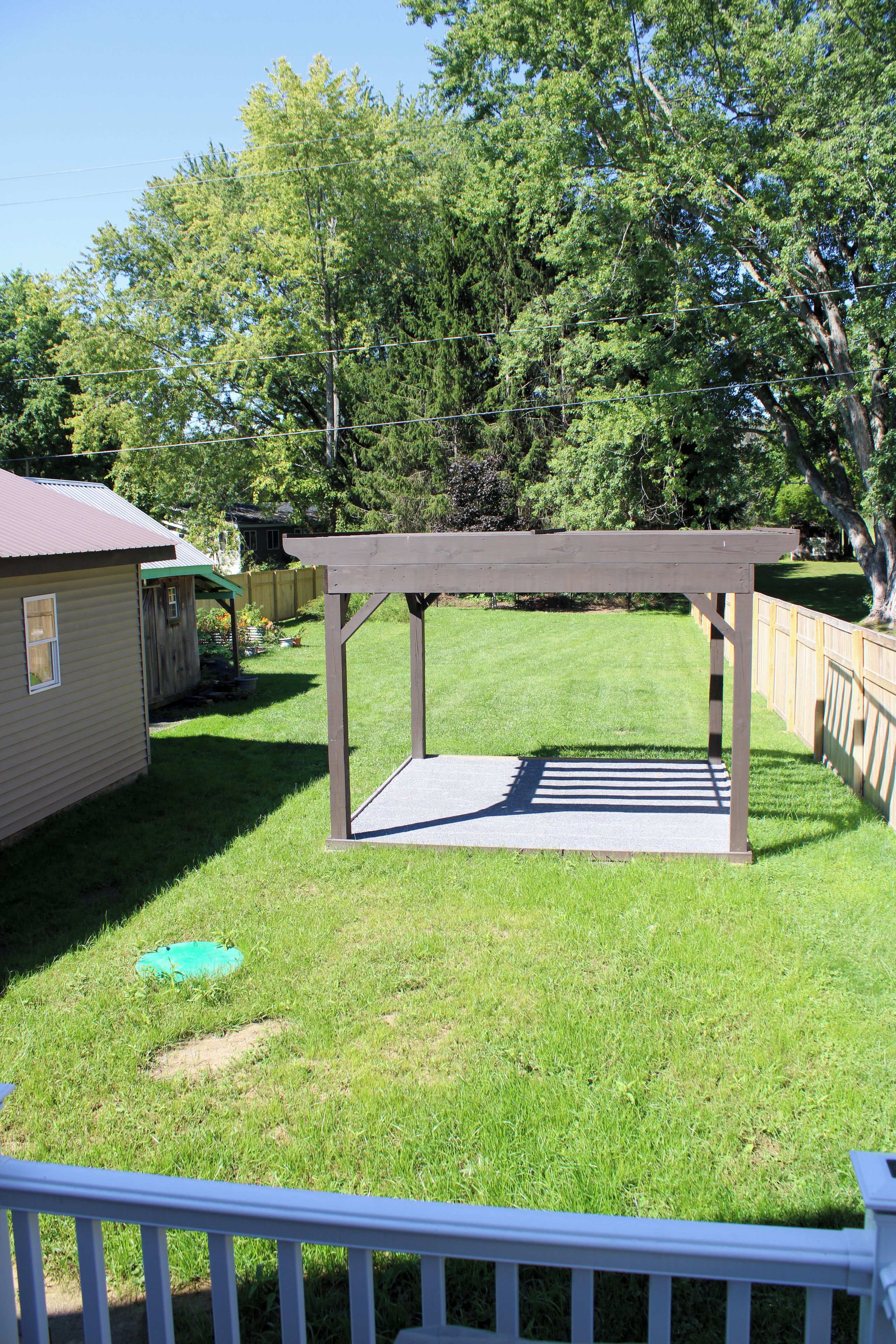 A backyard with a wooden pergola, a small shed, and a fenced area.