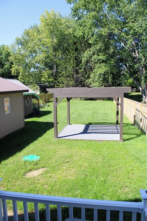 Patio trasero con un pérgola de madera, un cobertizo pequeño y una zona cercada.
