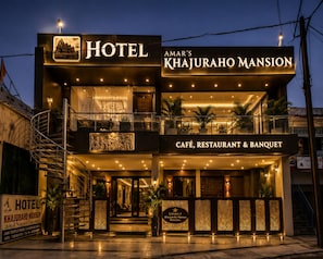 Un hotel con un cartel que indica que es 'Amar's Khajuraho Mansion' y cuenta con un café, restaurante y salón de banquetes.