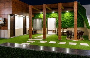 Un espacio exterior moderno con césped artificial, una zona de estar y una pared cubierta de follaje verde.