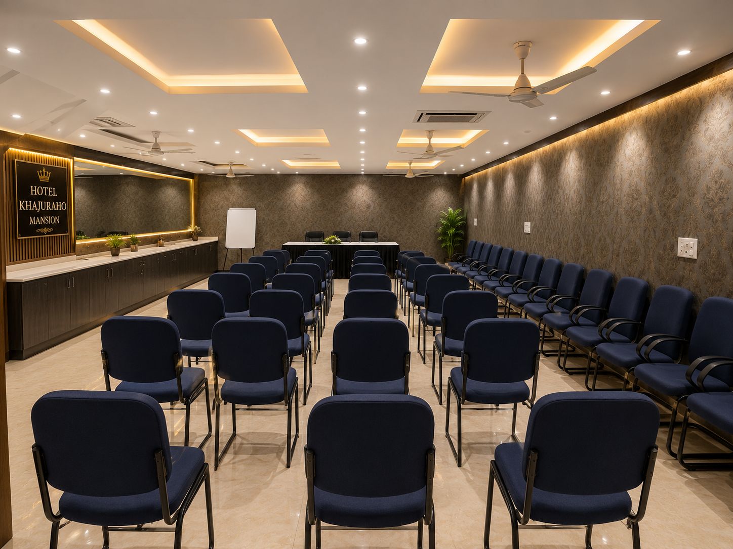 Un salón de conferencias de hotel con filas de sillas, un mostrador de recepción y ventiladores de techo.