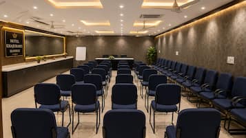 Un salón de conferencias de hotel con filas de sillas, un mostrador de recepción y ventiladores de techo.