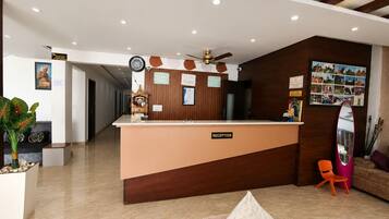 Ein Empfangsbereich mit einer Rezeption, einer Uhr, einem Deckenventilator und einer Wand mit gerahmten Fotos.