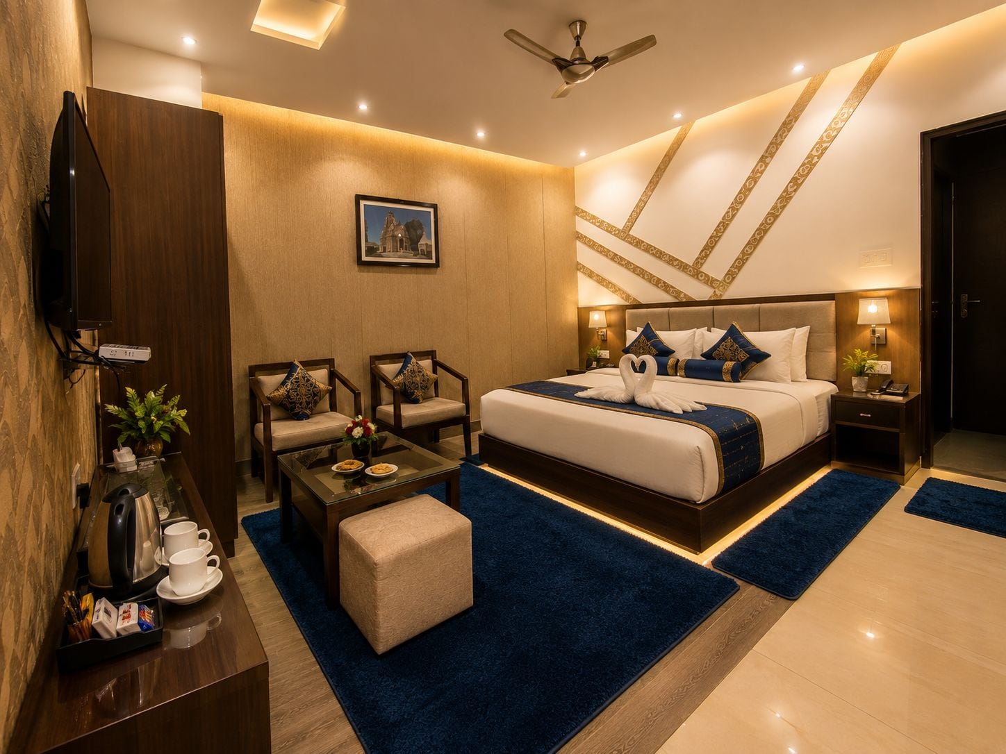 Una habitación de hotel moderna con una cama grande, dos sillones, una mesa de centro, un televisor y un escritorio con una planta y tazas de café.