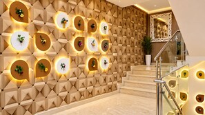 Un interior moderno con un muro de diseño geométrico, una escalera con barandilla de vidrio y macetas con flores iluminadas y fijadas a la pared.