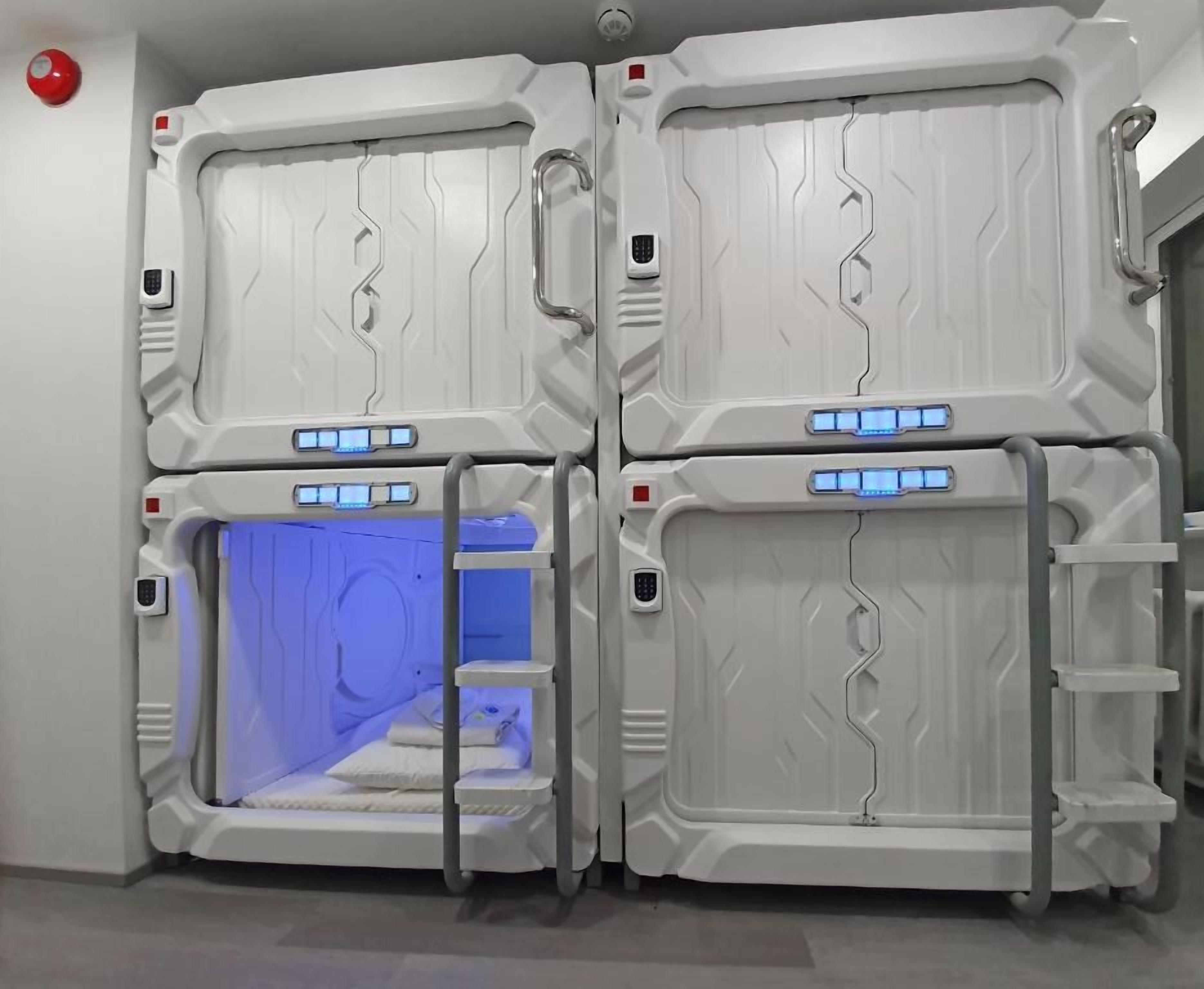 Una habitación con cuatro camas dispuestas en forma de cuadrado, cada una con un panel de control y una zona iluminada en azul.