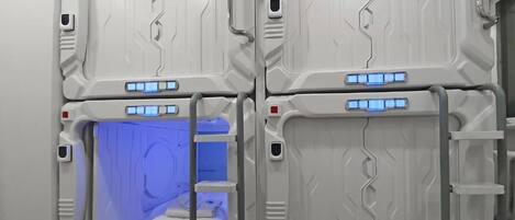 Una habitación con cuatro camas dispuestas en forma de cuadrado, cada una con un panel de control y una zona iluminada en azul.