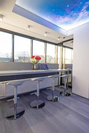 En moderne bar med udsigt over byen, et loft dekoreret med et stjerneskudsmotiv, og en vase med blomster på disken.