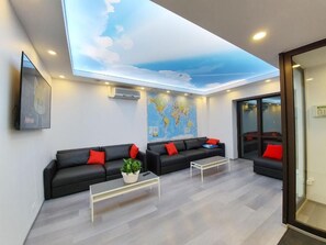 Un área de espera moderna con un mural en el techo, un mapa del mundo, sofás negros con cojines rojos y una mesa de centro.