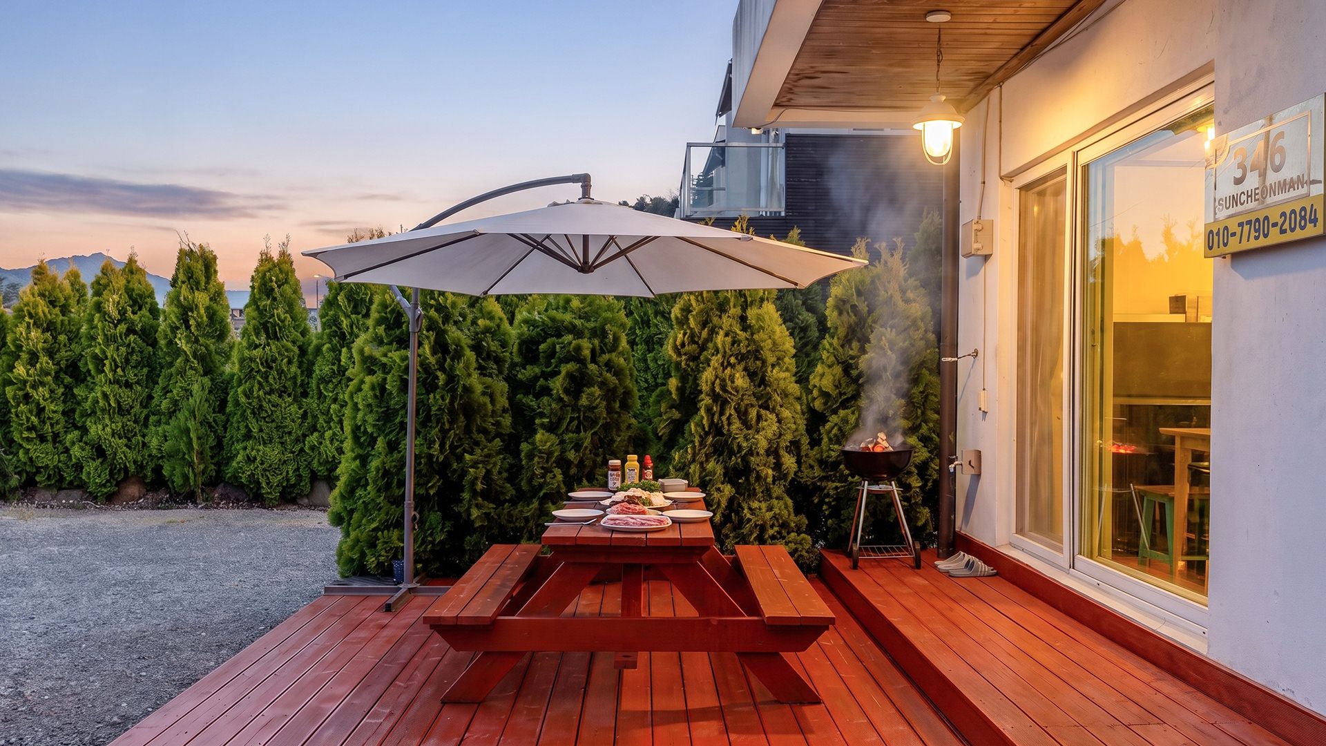 An outdoor patio with a wooden table and benches, a barbecue grill, and a large umbrella.
