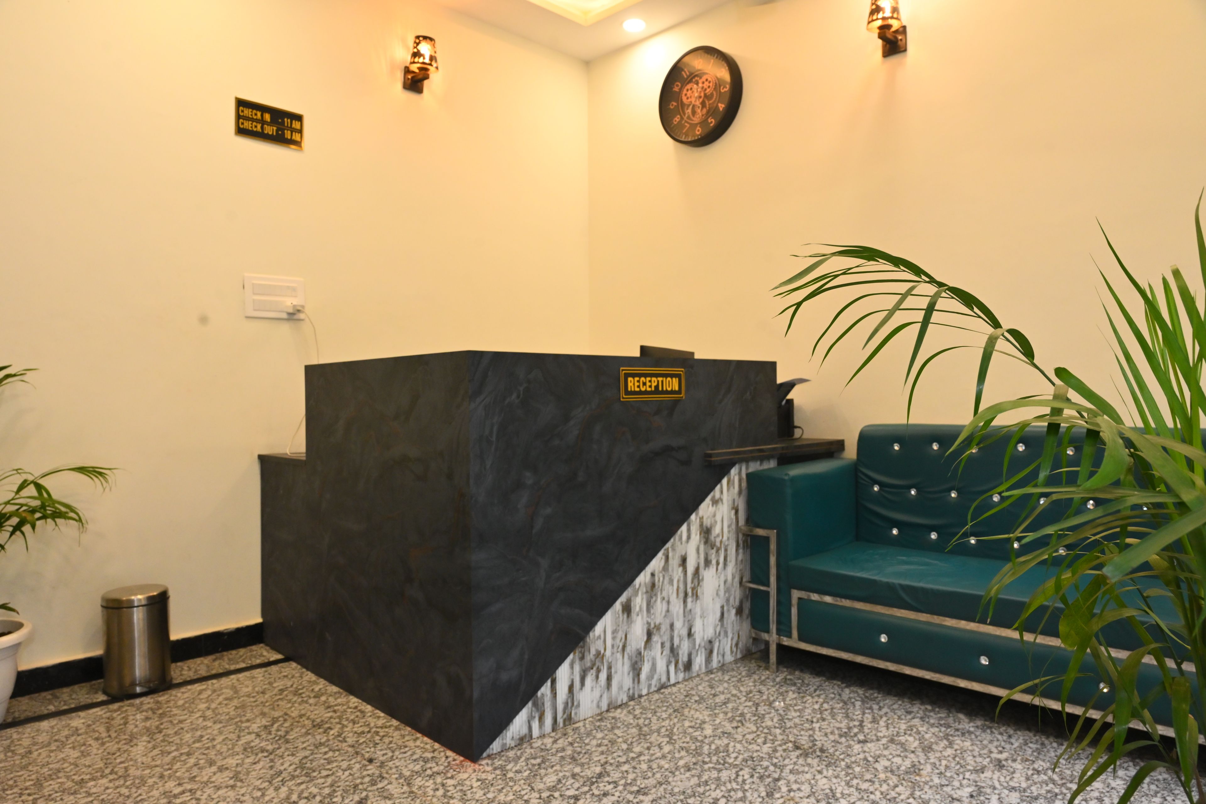 Uma área de recepção com balcão de mármore, um sofá verde-água e um relógio de parede.