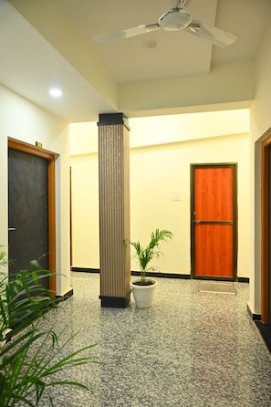 A hallway with a ceiling fan, a column, and a potted plant. - The Kashi Dham (Varanasi)