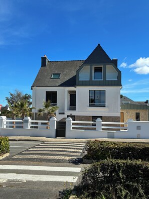A two-story house with a white exterior, a black roof, and a gated driveway.
