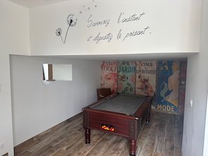 Una sala de billar con mesa de pool, un ventanal pequeño y un mural con texto e imágenes franceses.