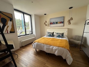Un dormitorio con una cama, una ventana, un radiador, una silla y un cuadro en la pared.